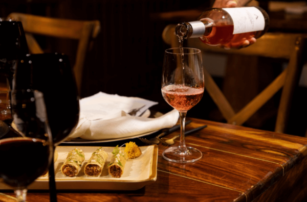 waiver pours rose wine with appetizer food on table