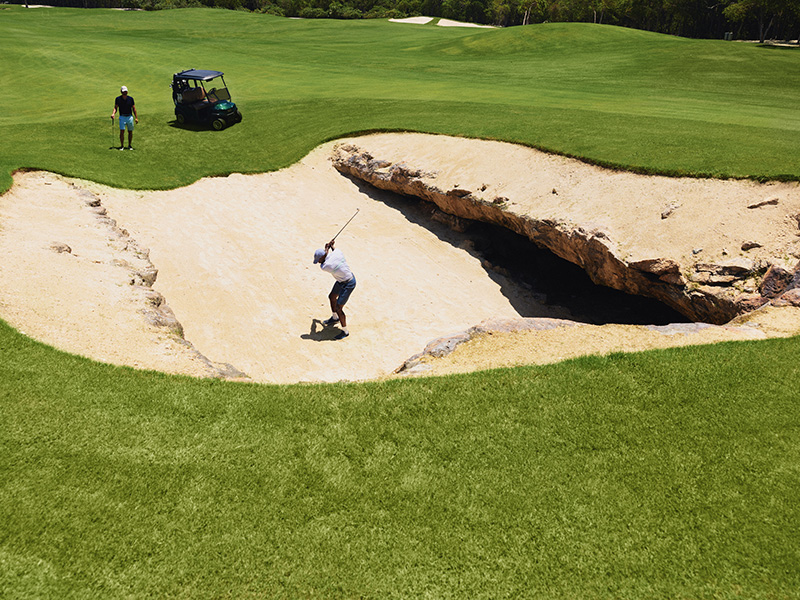 golfer swings from san dune of cenote hole at mayakoba