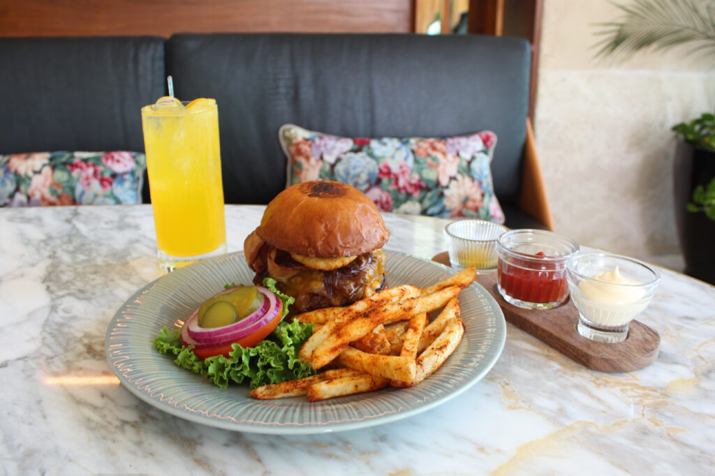 hamburguer with french fries, and an orange drink to the side over a table