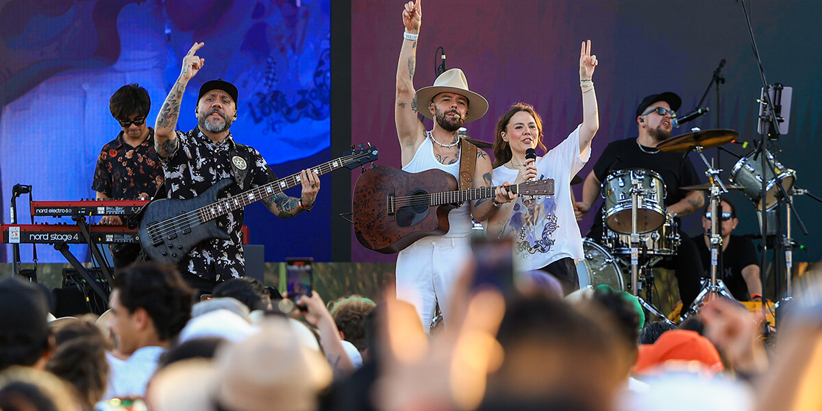 singers raise hands on stage with large outdoor audience